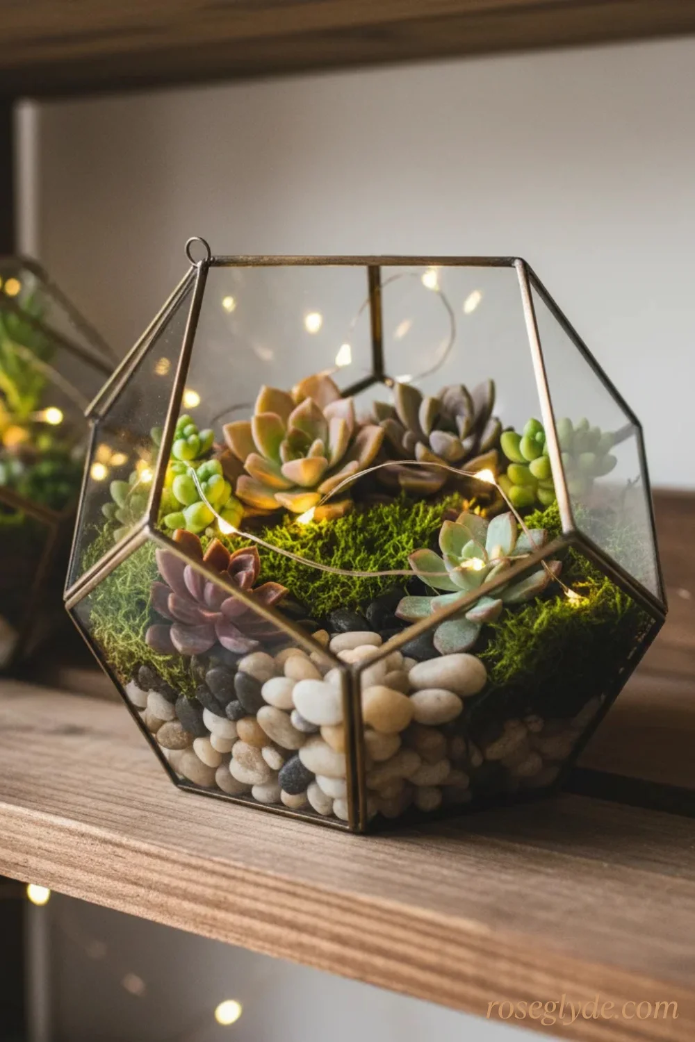 A geometric glass terrarium with plants and fairy lights on a wooden shelf.