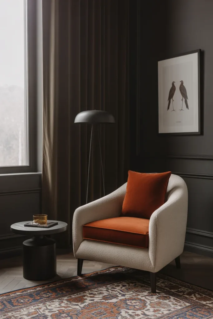 A cozy reading nook featuring an armchair with an orange seat cushion and a small side table next to a window Graphite Walls.